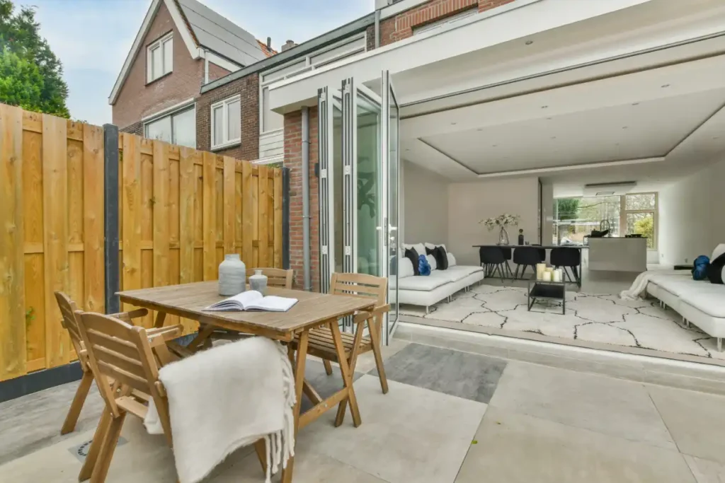 Seamless transition between outdoor patio with wooden table and chairs and modern open-plan living area