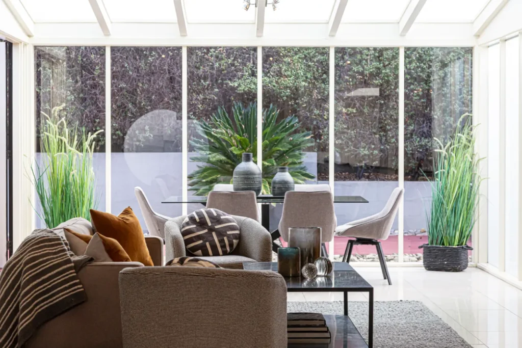 Bright modern conservatory with glass roof, beige chairs, and decorative plants