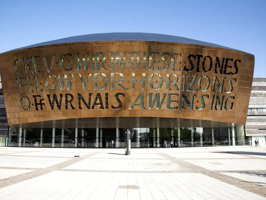 Curved building facade with large cut-out text in Welsh and English under a clear blue sky