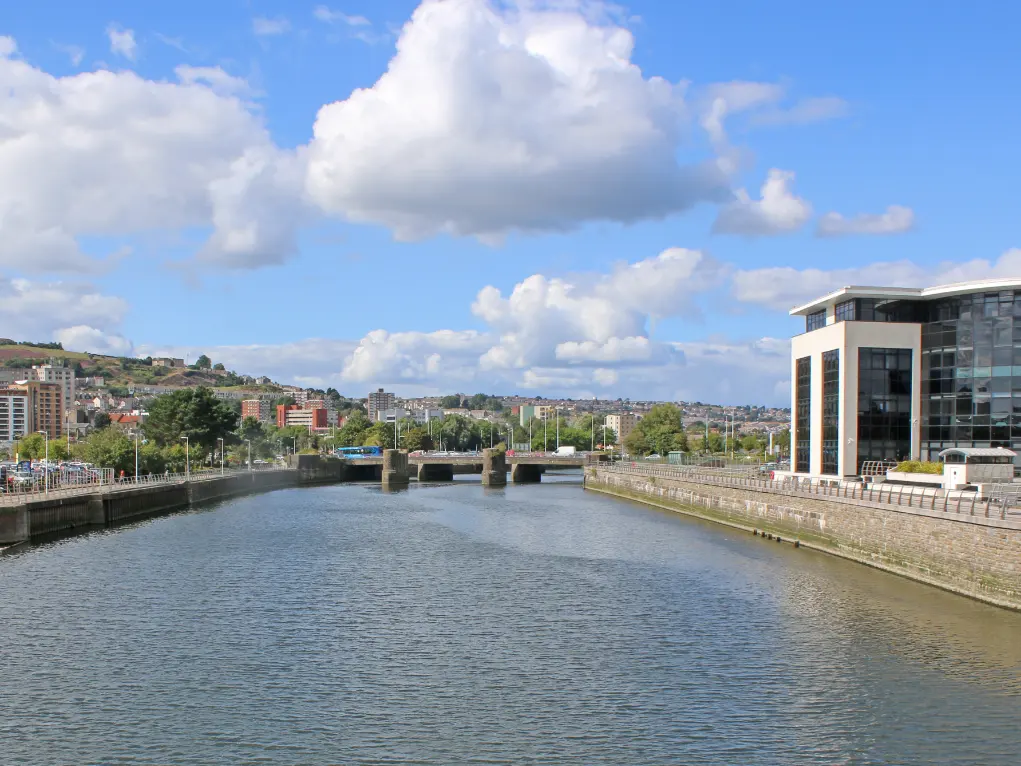 River through Swansea cityscape with buildings and hills under a partly cloudy sky